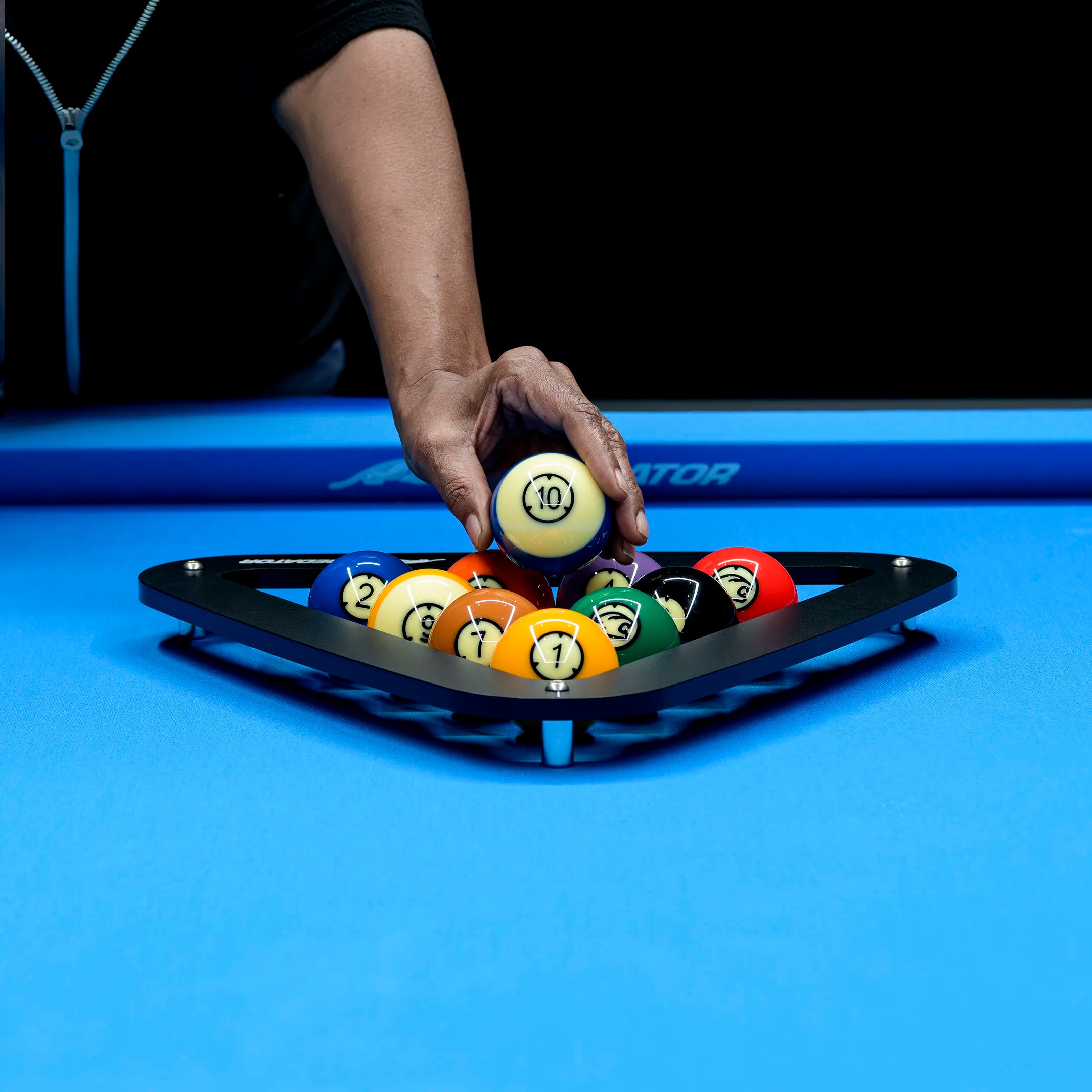 Hand picking a billiard ball from a black pool ball rack on a blue felt pool table.