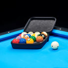Set of pool balls in a black case on a pool table with a blue surface.