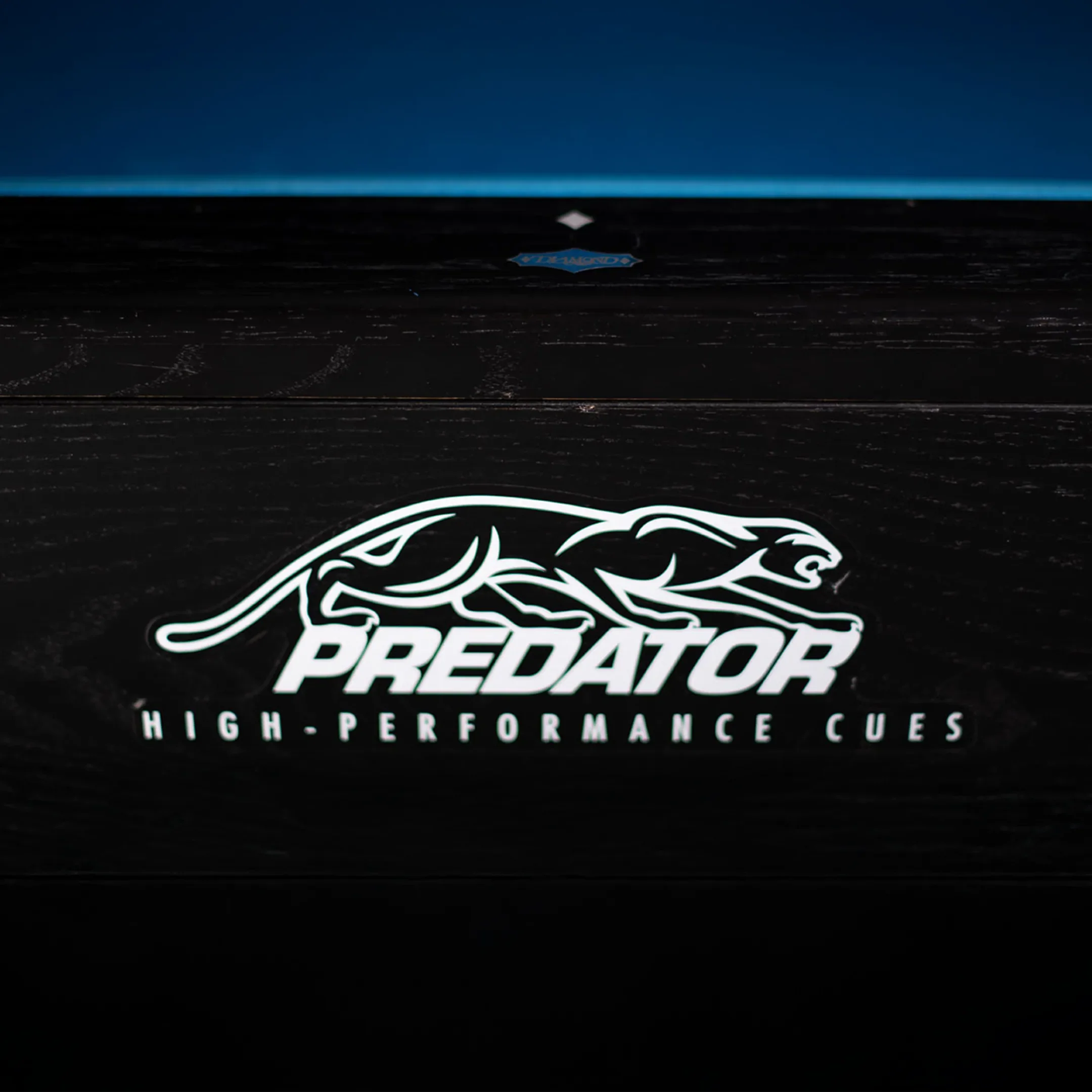 White cat logo with text: PREDATOR High-Performance Cues. Logo on wooden pool table. 