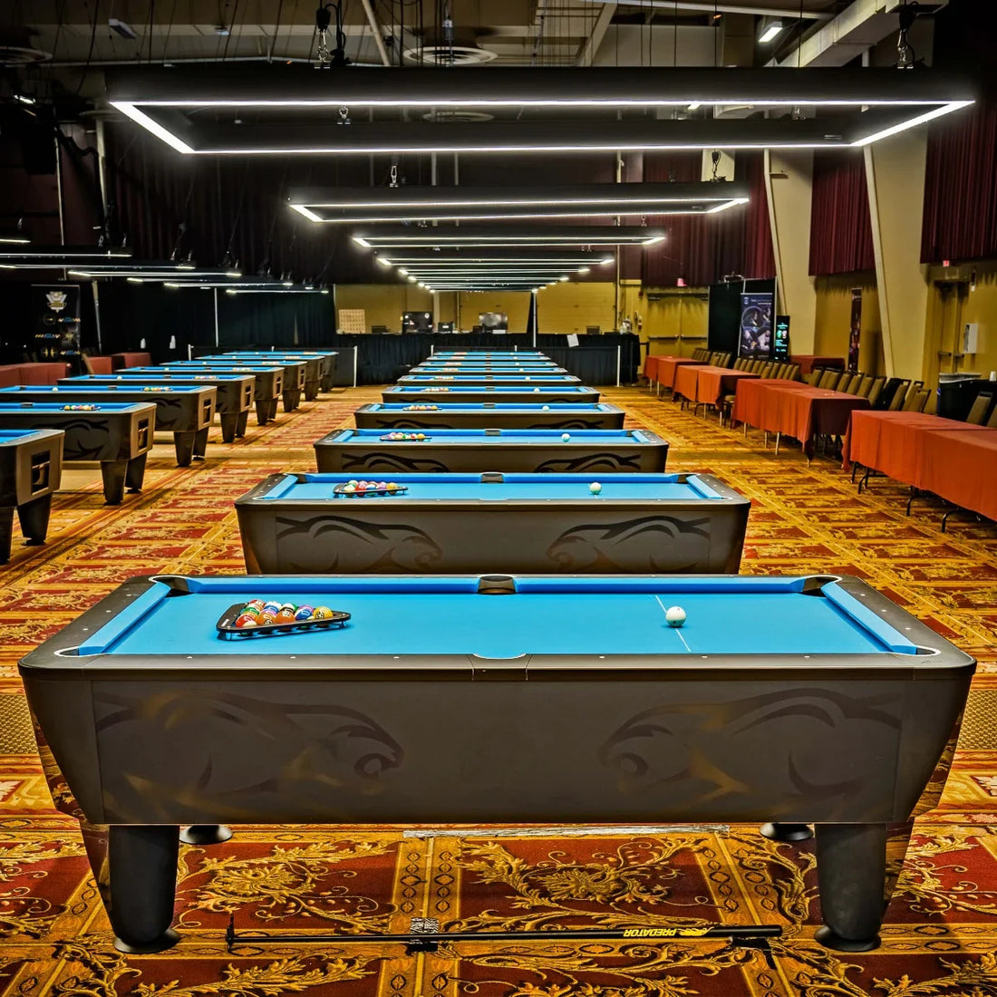 Multiple pool tables arranged in a large indoor area with a patterned carpet